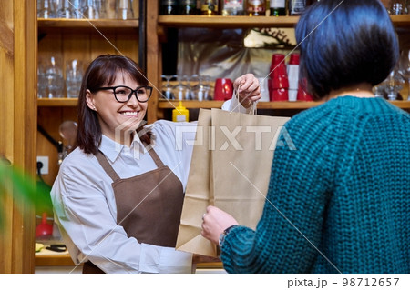 Woman restaurant worker issuing an order for takeaway food in paper bag Woman restaurant worker issuing an order for takeaway food in paper bag 98712657