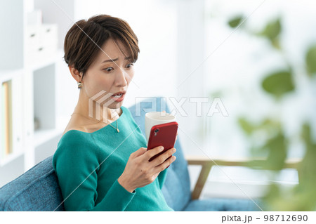 スマホを使うミドル女性（驚く・びっくり・ショック） 98712690