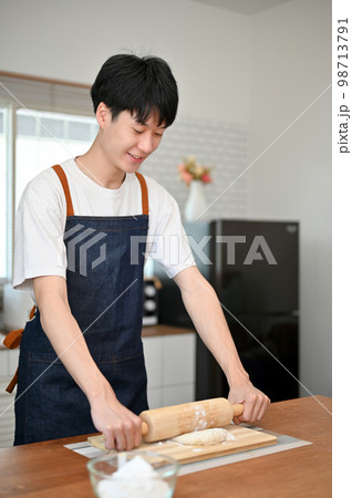 Handsome Asian man wearing apron kneading dough with a rolling pin, making dough 98713791