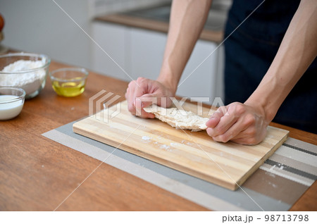 Close-up hand image of a male baker kneading raw dough, making homemade pastry at home. 98713798