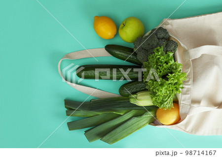 Net bag with fruits and vegetables on turquoise background, flat lay 98714167