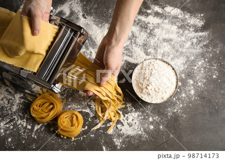 Woman preparing noodles with pasta maker machine at grey table, top view Woman preparing noodles with pasta maker machine at grey table, top view 98714173