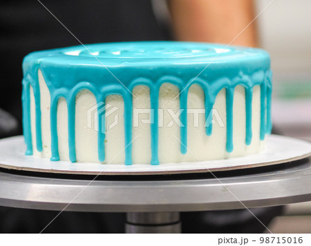 hand pastry chef designer topping a frosted white cake with pastel light blue drip filling bag hand pastry chef designer topping a frosted white cake with pastel light blue drip filling bag 98715016