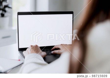 Woman hands typing on the laptop with empty blank white screen mockup. Computer is laying on the white table. Blurred background. Person working from home concept. Copy space area for text 98715609