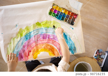 Confident cute male kid art drawing multicolored rainbow arch use paints and brush on table 98716235