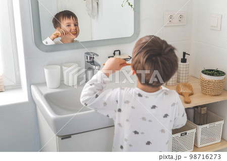 Cute male kid in pajamas cleaning teeth with eco friendly toothbrush comfortable minimalist bathroom Cute male kid in pajamas cleaning teeth with eco friendly toothbrush comfortable minimalist bathroom 98716273
