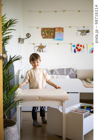 Smiling baby boy playing at cozy childish playroom interior with paper sheet rainbow arch drawing 98716314