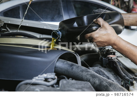 Car mechanic replacing and pouring fresh oil into engine at maintenance repair service station, 98716574