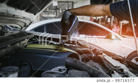 Car mechanic replacing and pouring fresh oil into engine at maintenance repair service station, 98716577