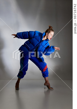 Fashion portrait of young beautiful woman in retro style trousers and winter down jacket posing over gray background. Seasons fashion, vintage, 70s, 80s style 98716742