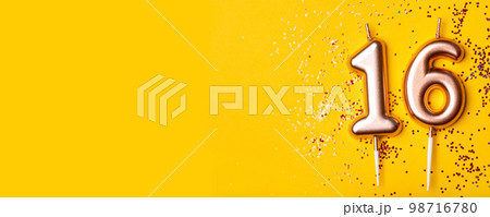 Gold candles in the form of number sixteen on yellow background with confetti. 16 years celebration. Gold candles in the form of number sixteen on yellow background with confetti. 16 years celebration. 98716780