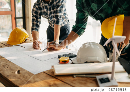 Two colleagues discussing data working and tablet, laptop with on on architectural project at construction site at desk in office 98716913
