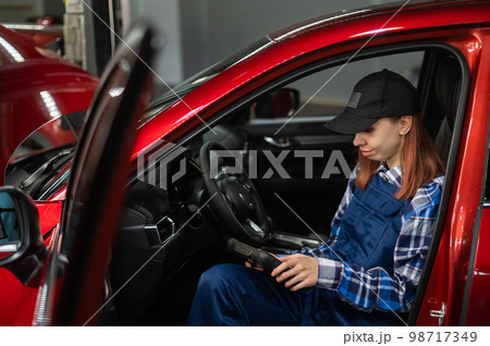 Caucasian female auto mechanic uses a special computer to diagnose faults. Caucasian female auto mechanic uses a special computer to diagnose faults. 98717349