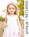 Cute happy baby girl 2-3 year old walking in meadow on green background. Smiling child. Childhood. Looking at camera. 98718000
