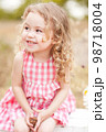 Funny baby girl 2-3 year old  sitting in meadow outdoors. Laughing child. Looking away. Childhood. 98718004