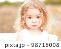 Cute baby girl with blonde curly hair outdoors. Little girl 2-3 year old. 98718008