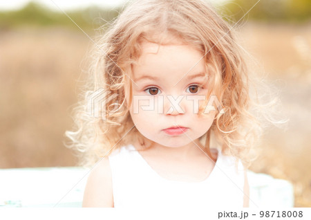 Cute baby girl with blonde curly hair outdoors. Little girl 2-3 year old. 98718008