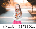 Cute baby girl 5-6 year old holding autumn leaves in park. Looking at camera. Childhood. 98718011