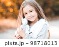 Smiling baby girl 4-5 year old holding handmade toy rabbit outdoors. Looking at camera. Childhood. 98718013