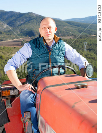 Confident male owner of vineyard driving tractor outdoors in sunny day Confident male owner of vineyard driving tractor outdoors in sunny day 98718852