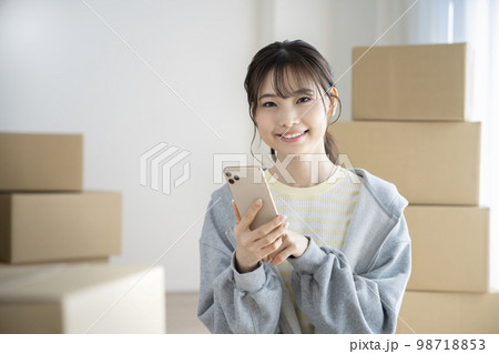 スマートフォンを持ったカメラ目線で笑顔の若い女性　引越しイメージ 98718853