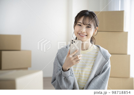 スマートフォンを持ったカメラ目線で笑顔の若い女性　引越しイメージ 98718854