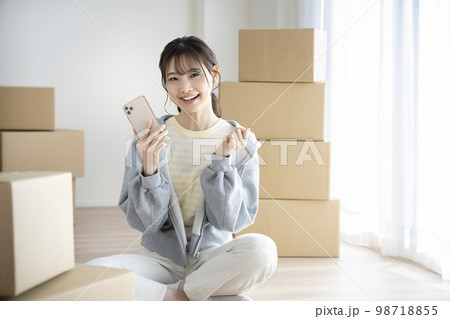 スマートフォンを持ったカメラ目線で笑顔の若い女性　引越しイメージ 98718855