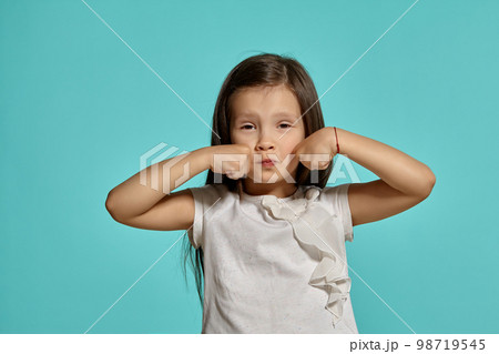Close-up studio shot of beautiful brunette little girl posing against a blue background. Close-up studio shot of beautiful brunette little girl posing against a blue background. 98719545