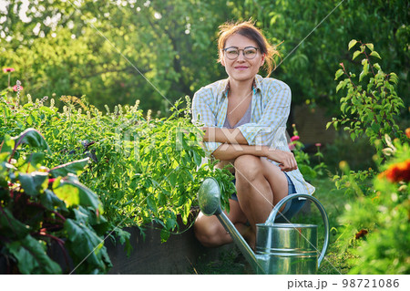 Middle-aged woman with watering can near garden bed with spicy fragrant herbs 98721086