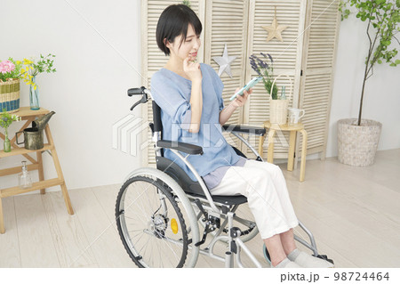 家でスマホを使う車椅子に乗った障がい者女性 98724464
