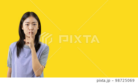 Asian woman doing silent gesture with finger, Noiseless symbol, Noisy mall, Hide a secret, Do not speak. shut your mouth, Noiseless signal transmission, Isolated on yellow background. Asian woman doing silent gesture with finger, Noiseless symbol, Noisy mall, Hide a secret, Do not speak. shut your mouth, Noiseless signal transmission, Isolated on yellow background. 98725069