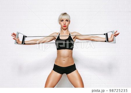Slim young blond sportive woman doing exercises with expander while on white studio background Slim young blond sportive woman doing exercises with expander while on white studio background 98725235