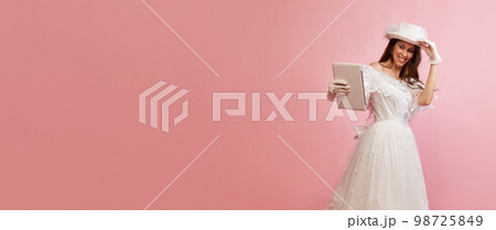 Modern devices. Video call. Portrait of beautiful lady in white vintage dress posing with tablet over pink background. Concept of 19th century, fashion, comparison of eras Modern devices. Video call. Portrait of beautiful lady in white vintage dress posing with tablet over pink background. Concept of 19th century, fashion, comparison of eras 98725849