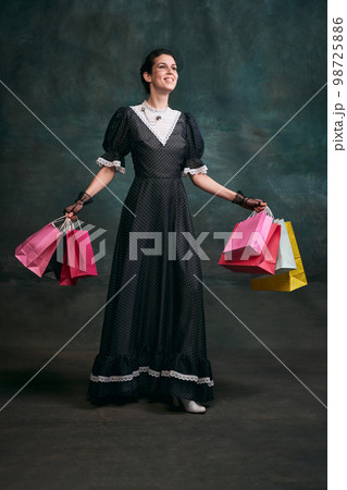 Shopping. Young beautiful woman in image of Anna Karenina in retro black dress posing over dark vintage background. Sales. Concept of literature character, history 98725886
