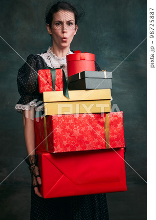 With present boxes. Young beautiful woman in image of Anna Karenina in retro black dress posing over dark vintage background. Concept of literature character, history With present boxes. Young beautiful woman in image of Anna Karenina in retro black dress posing over dark vintage background. Concept of literature character, history 98725887