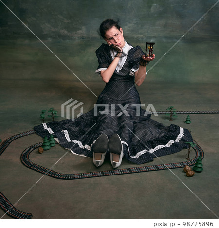 Waiting. Young beautiful woman in image of Anna Karenina in retro black dress posing around toy over dark vintage background. Concept of literature character, history 98725896