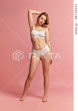 Studio shot of young slim woman wearing white inner wear posing over pink color background. Concept of natural beauty, body and skin care, healthy eating Studio shot of young slim woman wearing white inner wear posing over pink color background. Concept of natural beauty, body and skin care, healthy eating 98726345