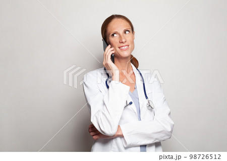 Beautiful doctor mid adult woman wearing white medical uniform using smartphone Beautiful doctor mid adult woman wearing white medical uniform using smartphone 98726512