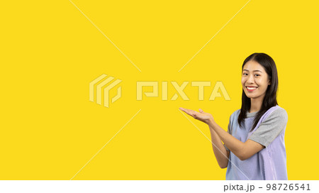 Asian woman with holding copyspace imaginary on the palm to insert an ad, Showing copyspace pointing, Showing her hand to present something on yellow background. 98726541