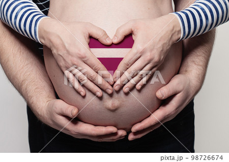 Latvian family concept. Man embracing pregnant woman belly and heart with flag of Latvia Latvian family concept. Man embracing pregnant woman belly and heart with flag of Latvia 98726674