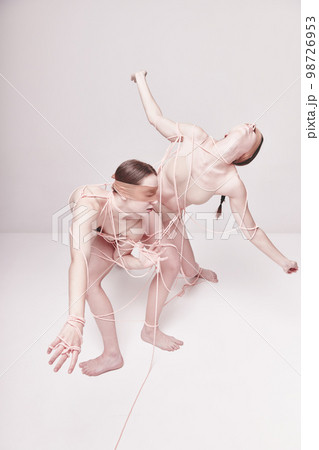 Freedom. Portrait of two young girls posing in underwear and ropes with eyes closed over light studio background. Concept of weird people, contemporary photography 98726953