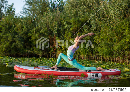 Young woman are doing yoga on a stand up paddle board SUP on a beautiful lake or river Young woman are doing yoga on a stand up paddle board SUP on a beautiful lake or river 98727662