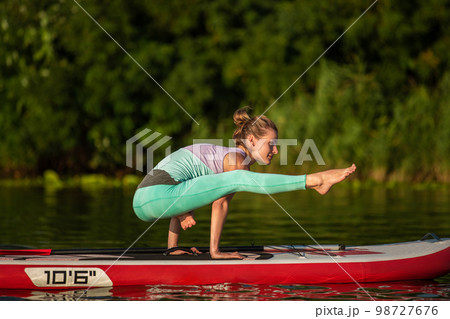 Young woman are doing yoga on a stand up paddle board SUP on a beautiful lake or river 98727676