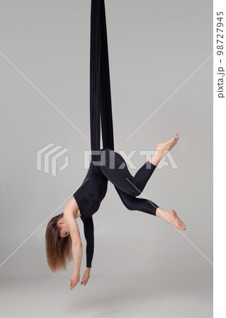 Beautiful girl in a black sport suit is performing an acrobatic elements in a studio. Beautiful girl in a black sport suit is performing an acrobatic elements in a studio. 98727945