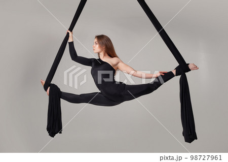 Beautiful girl in a black sport suit is performing an acrobatic elements in a studio. Beautiful girl in a black sport suit is performing an acrobatic elements in a studio. 98727961