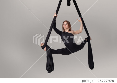 Beautiful girl in a black sport suit is performing an acrobatic elements in a studio. Beautiful girl in a black sport suit is performing an acrobatic elements in a studio. 98727970