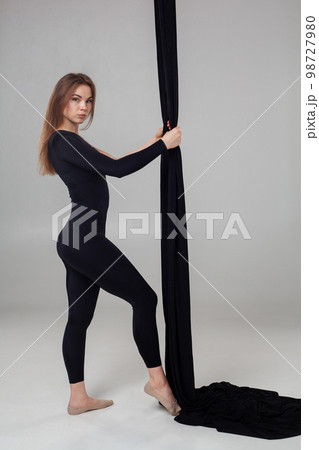 Beautiful girl in a black sport suit is performing an acrobatic elements in a studio. Beautiful girl in a black sport suit is performing an acrobatic elements in a studio. 98727980