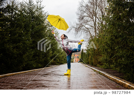 Coping with stress and anxiety. Practicing mindfulness and relaxation techniques. Happy senior woman in yellow rain coat with yellow umbrella walking and enjoying life in rainy park 98727984