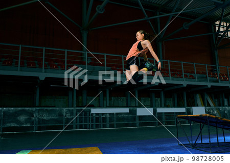 Rollerblader jump high from big air ramp performing trick. Indoors skate park equipment. 98728005