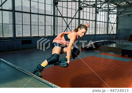 Rollerblader jump high from big air ramp performing trick. Indoors skate park equipment. 98728013